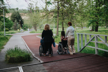 Two caregivers accompany a child in a wheelchair along a park pathway, showcasing outdoor support...