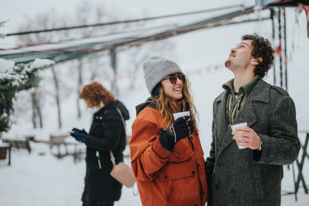 Two cheerful friends enjoying warm drinks during a snowy winter day outdoors