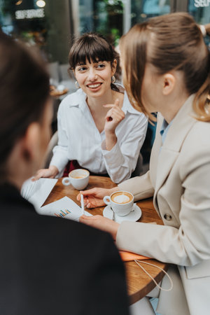 Three businesswomen having a friendly conversation at a cafe, discussing documents and ideas.の写真素材
