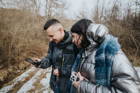 Two friends enjoying a moment outdoors while sharing a laugh and using their phone during a hike on...