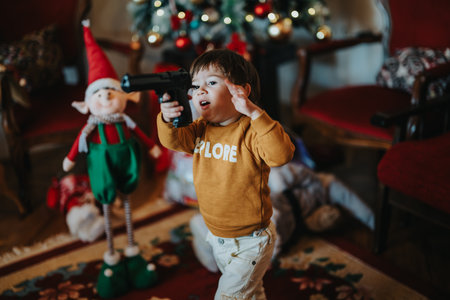 Child playing indoors near a festive Christmas tree, holding a toy and expressing excitement during...
