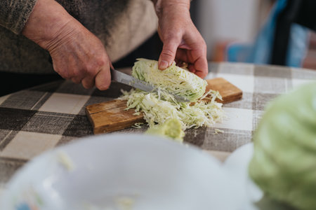 Senior person chopping fresh cabbage on a wooden board in a rustic kitchen