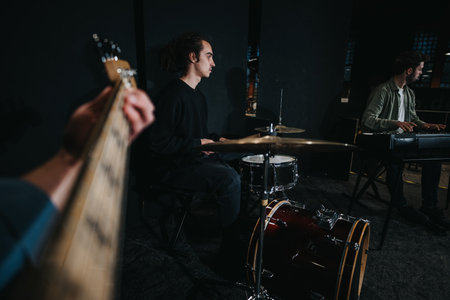 Musicians practicing as a band with drums and guitar in a dimly lit studioの写真素材