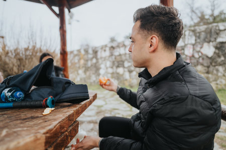 Person resting at a wooden picnic table with a backpack and hiking pole in an outdoor park setting.
