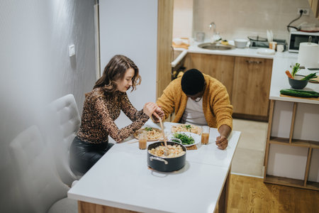 Two individuals share a delicious meal at a cozy home dining table in a modern kitchen settingの写真素材