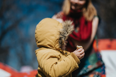 Child in a yellow winter coat enjoying outdoor time with an adult in the background during a clear...