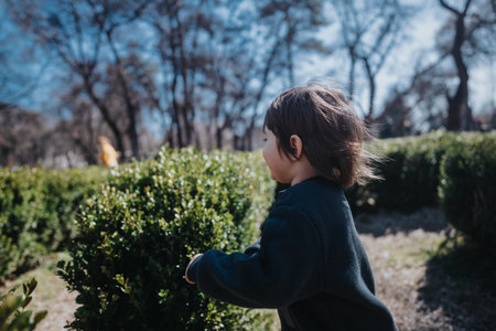 Young child playing in a sunny outdoor park surrounded by green hedges and trees