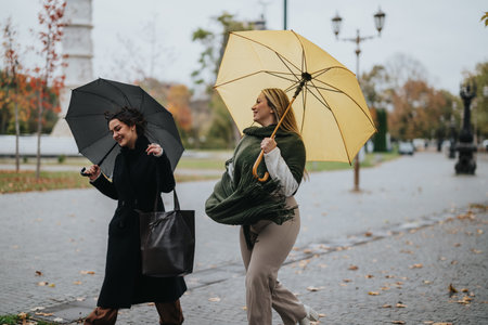 Two women walking outdoors with umbrellas on a breezy autumn day