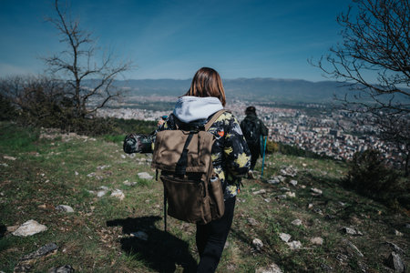 Two individuals hiking downhill on a sunny day overlooking a scenic cityscape from the vantage of a rocky hillside.の写真素材