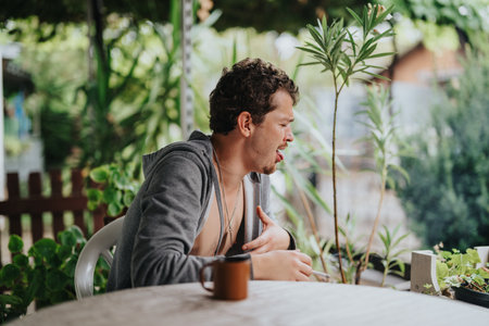Young man enjoying a relaxed moment at an outdoor patio surrounded by lush green foliageの写真素材