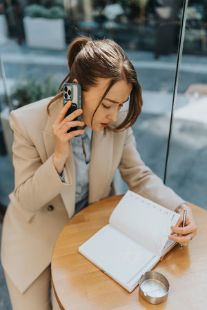 Female entrepreneur managing tasks with a phone call and planner at a cafe