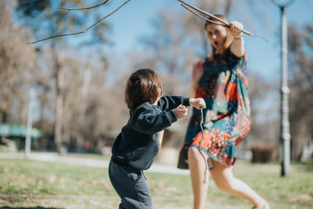 Children playing outdoors at a park with sticks during a sunny day, showcasing an energetic and playful childhood moment.の写真素材