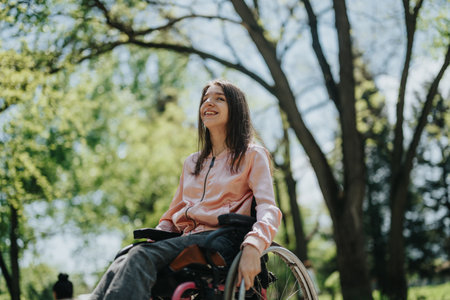 Young woman in wheelchair enjoying a sunny day outdoors in a park surrounded by lush treesの写真素材