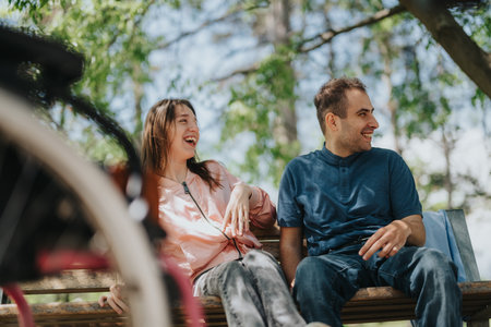 Two friends enjoying a sunny day sitting on a park bench and laughing together outdoors