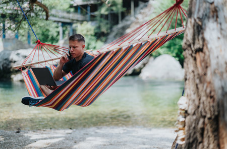 Person Working on a Laptop While Relaxing in a Hammock Outdoorsの写真素材