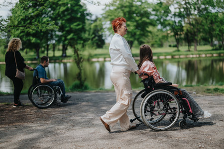 Two women assist wheelchair users during a serene outdoor visit to a park with a lakeの写真素材