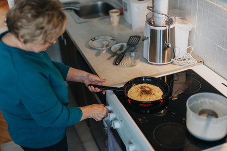 Senior woman preparing a pancake on a stove in a home kitchenの写真素材