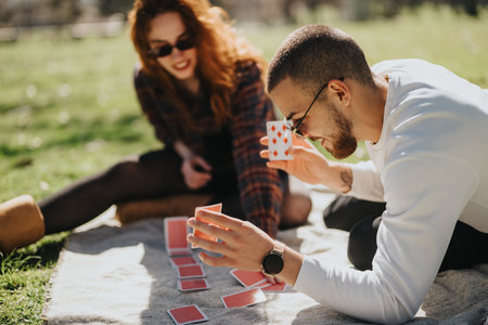 Couple enjoying a sunny day playing cards together in a parkの写真素材