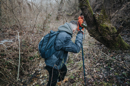 Two hikers traverse a natural forest trail during a cold season, showcasing adventure amidst the rugged terrain and bare trees.の写真素材