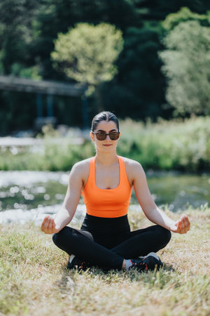 Woman practicing yoga beside a scenic river in sunlightの写真素材