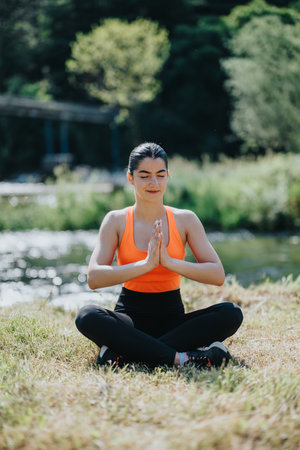 Woman practicing yoga meditation near a tranquil river in outdoor settingの写真素材