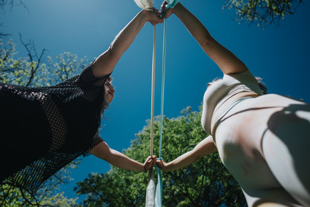Two friends interacting with fabric outdoors under clear skyの写真素材