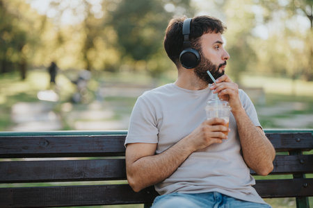 Man relaxing on a park bench with headphones and iced coffeeの写真素材