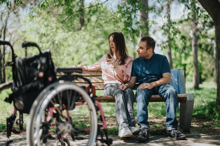 Couple enjoying time together on a park bench with a wheelchair nearby in a lush green park settingの写真素材