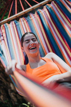 Relaxed woman smiling in a colorful hammock on a sunny day outdoorsの写真素材