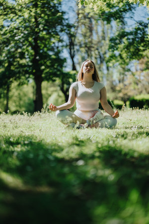 Young woman meditating outdoors on a sunny day with trees in the backgroundの写真素材