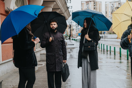 Diverse Group Meeting Outdoors Under Umbrellas on a Rainy Urban Dayの写真素材
