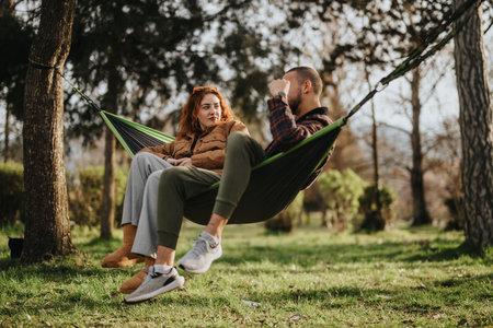 A couple enjoying a relaxing day outdoors in a hammock under the treesの写真素材
