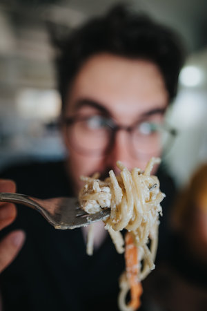 Person enjoying a delicious creamy spaghetti meal with focus on forkの写真素材