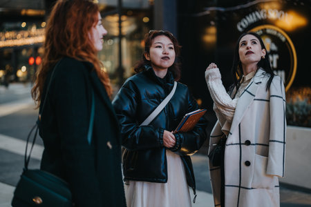 Three women interacting outdoors with a backdrop of urban evening lightsの写真素材