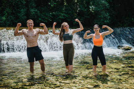 Group of friends smiling and flexing muscles in a natural water settingの写真素材