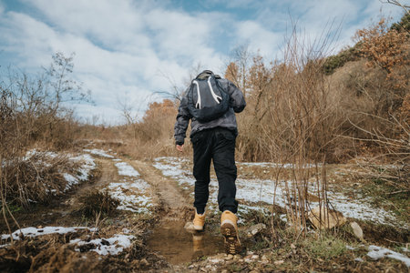 Hiker Exploring a Wintery Trail with Snowy Patches Under a Clear Blue Sky