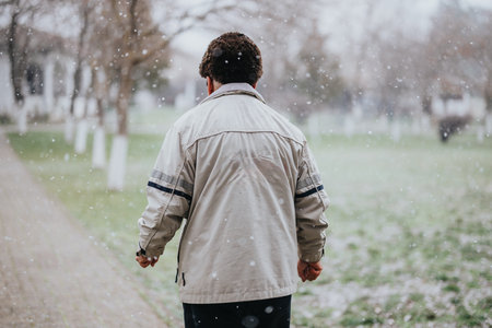 Senior man walking in a snowy park wearing a beige jacket with a number 15 print during winter seasonの写真素材