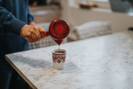 Senior man pours hot coffee into a decorated mug on a marble tableの写真素材