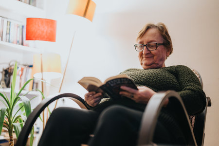 Elderly woman reading a book while sitting comfortably in an armchair at homeの写真素材