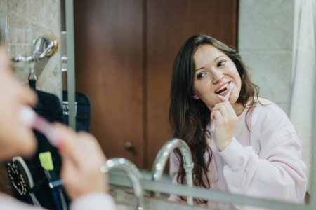 Young woman brushing her teeth in a bathroom while smiling into the mirrorの写真素材
