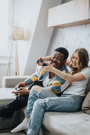 Couple enjoying video games together at home, sitting on cozy sofa in a bright living roomの写真素材
