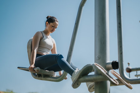 Woman exercising on outdoor fitness equipment in sunny parkの写真素材