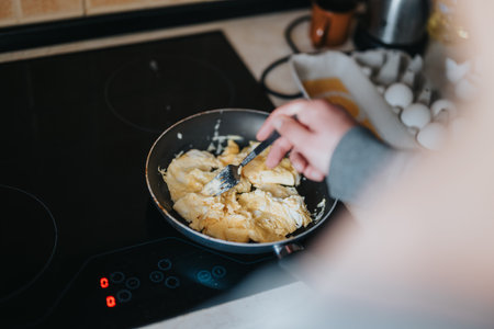 Person cooking scrambled eggs in a heated pan on an electric stove topの写真素材