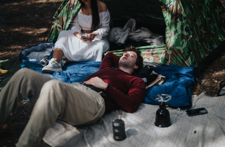 Friends relaxing near a tent while camping in a natural forest settingの写真素材