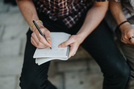Close-up of a person writing notes in a spiral notebook outdoorsの写真素材