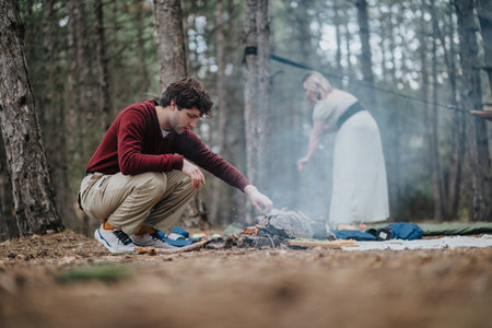 Man and woman enjoying camping in the woods, building campfire togetherの写真素材