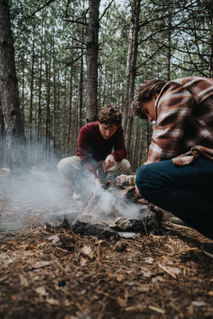 Two individuals building a campfire in a forest setting