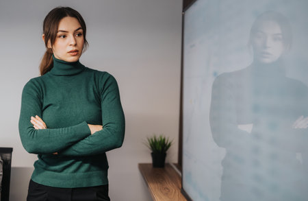 Professional woman standing in a modern office setting with a thoughtful expressionの写真素材