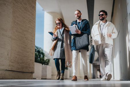 Three colleagues walking outdoors while discussing work and carrying documents