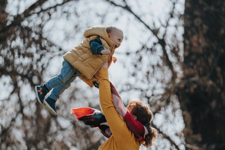 Mother lifting baby boy outdoors celebrating joy and love in a park on a sunny dayの写真素材
